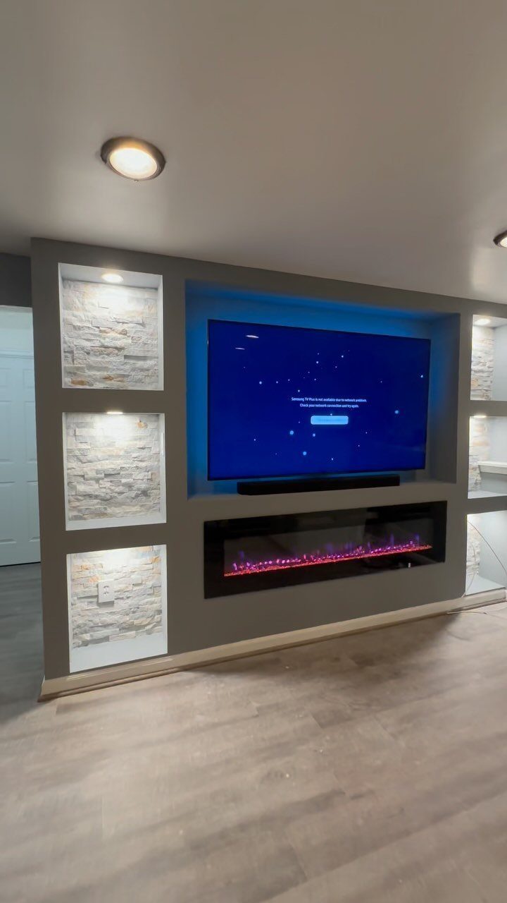 Modern electric fireplace with a large television mounted above it and stone niches.