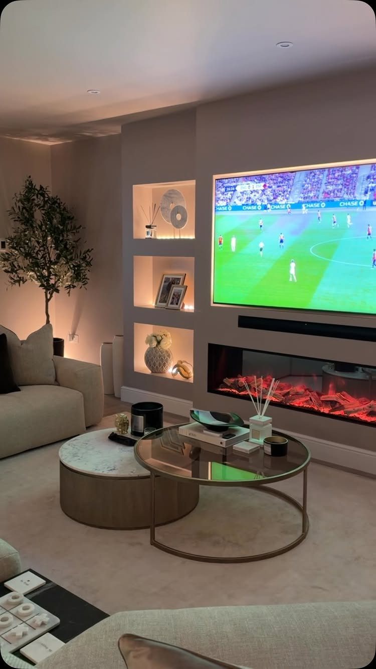 Built-in wall with a television above a linear electric fireplace and illuminated recessed shelving.