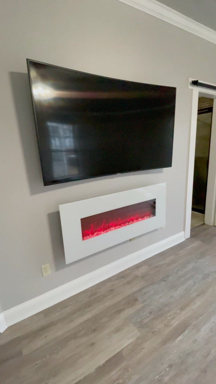 Curved flat-screen television mounted on a grey wall above a modern white electric fireplace.