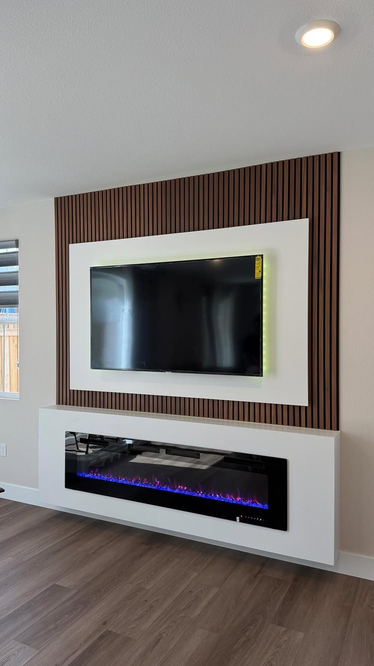 Linear electric fireplace with blue flames below a wall-mounted TV on wood slats.