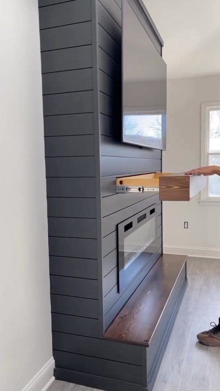 Dark grey shiplap fireplace wall with a mounted TV and a built-in wooden drawer.