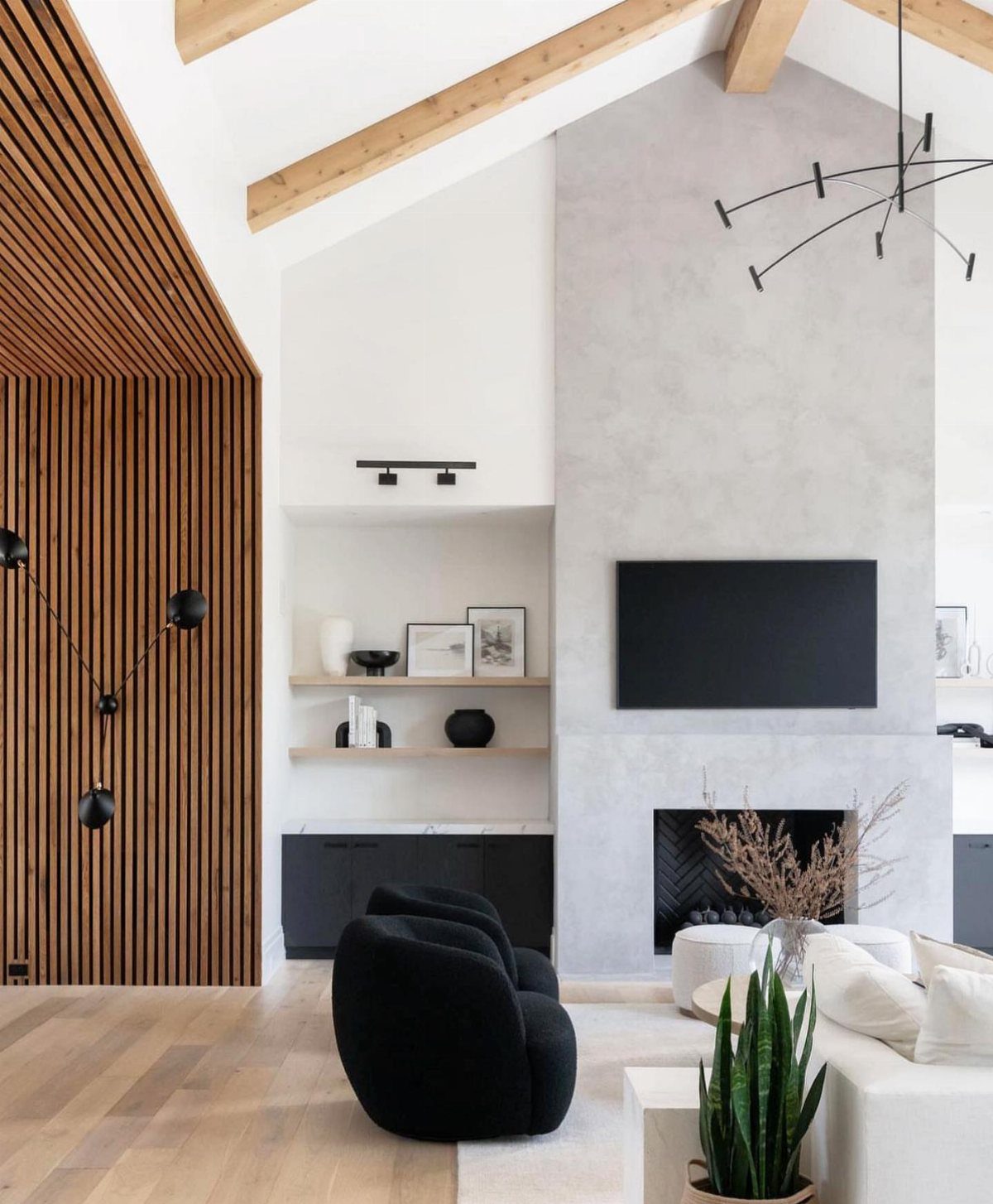 Grey concrete fireplace wall with TV under vaulted ceilings with exposed wooden beams.
