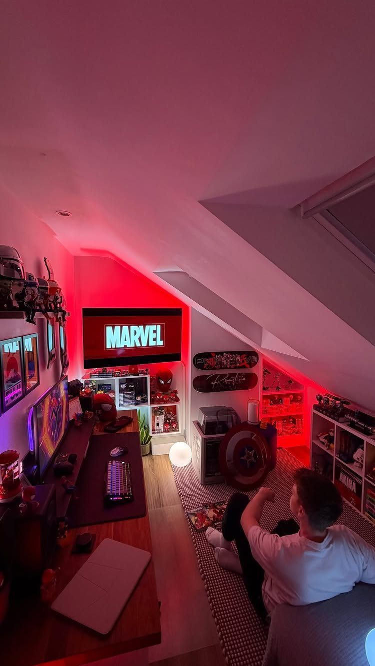 Gaming room in an attic with red lighting, computer desk, and Marvel themed decor.