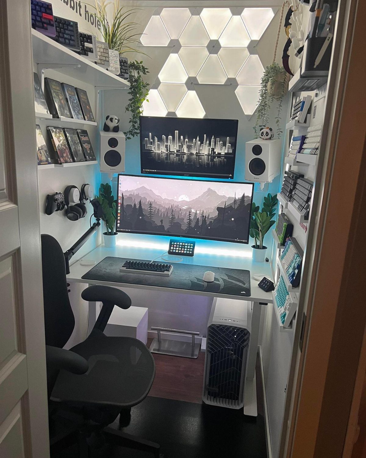 Compact gaming setup with dual monitors, hexagonal wall lights, and space-saving white furniture.