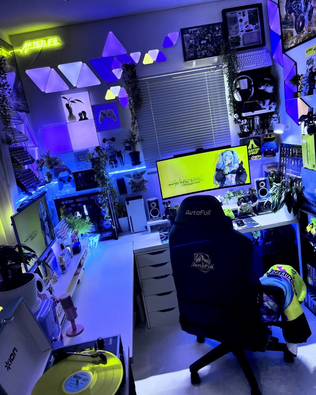 Gaming room with neon triangular wall lights, a black chair, and a computer setup.