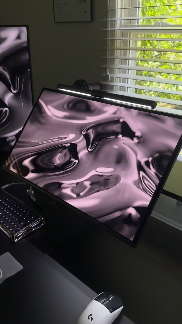 Two computer monitors with abstract pink art on a dark gaming desk.