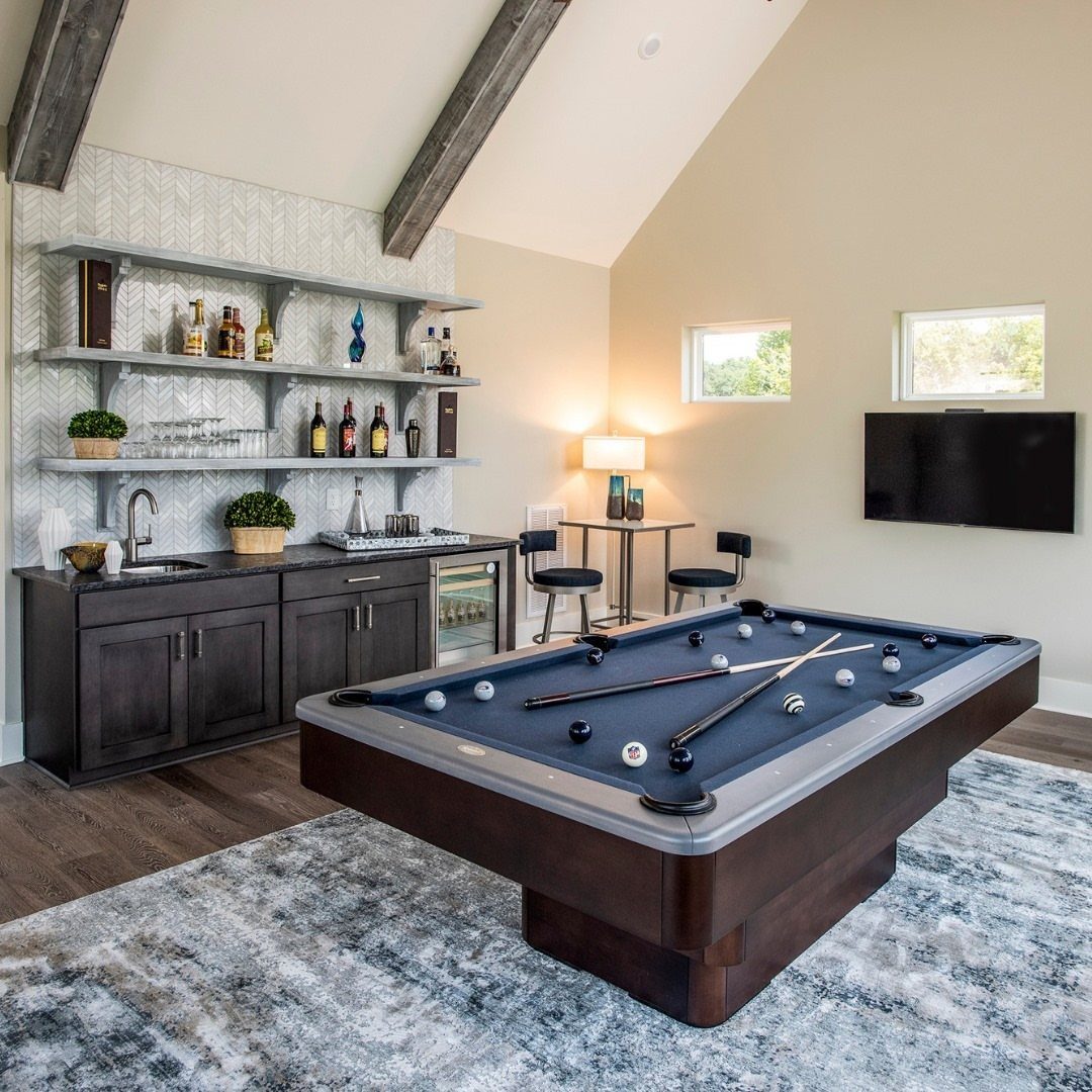 Blue pool table and dark wood wet bar in a spacious modern game room.