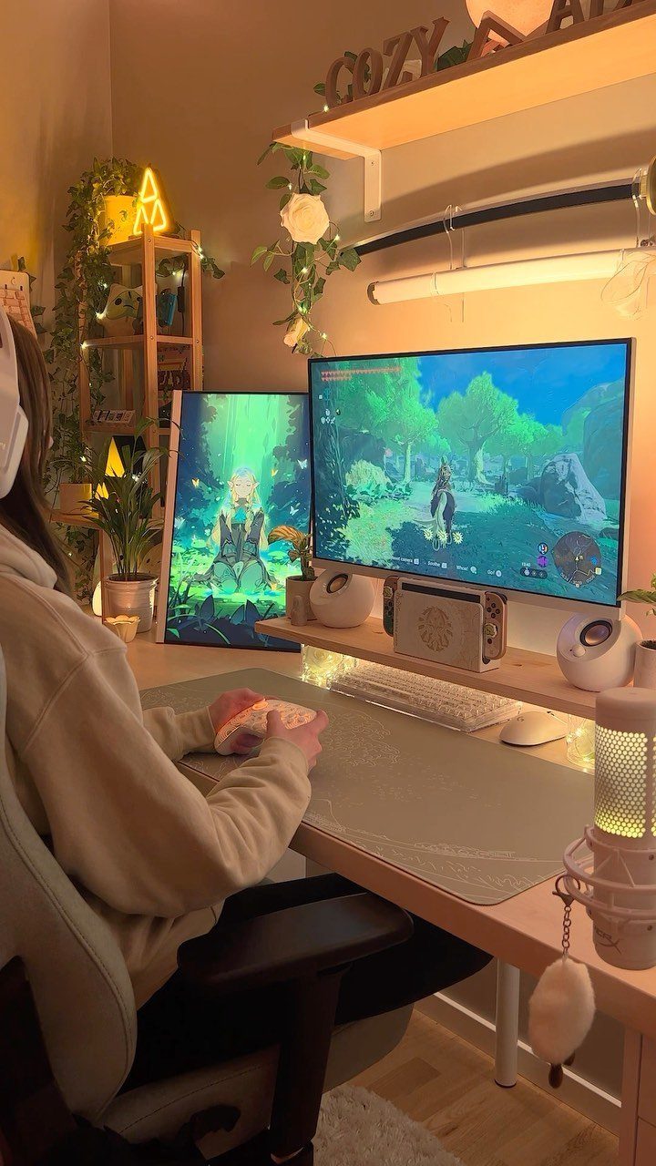 Person sitting at a dual monitor gaming setup with warm ambient lighting and plants.