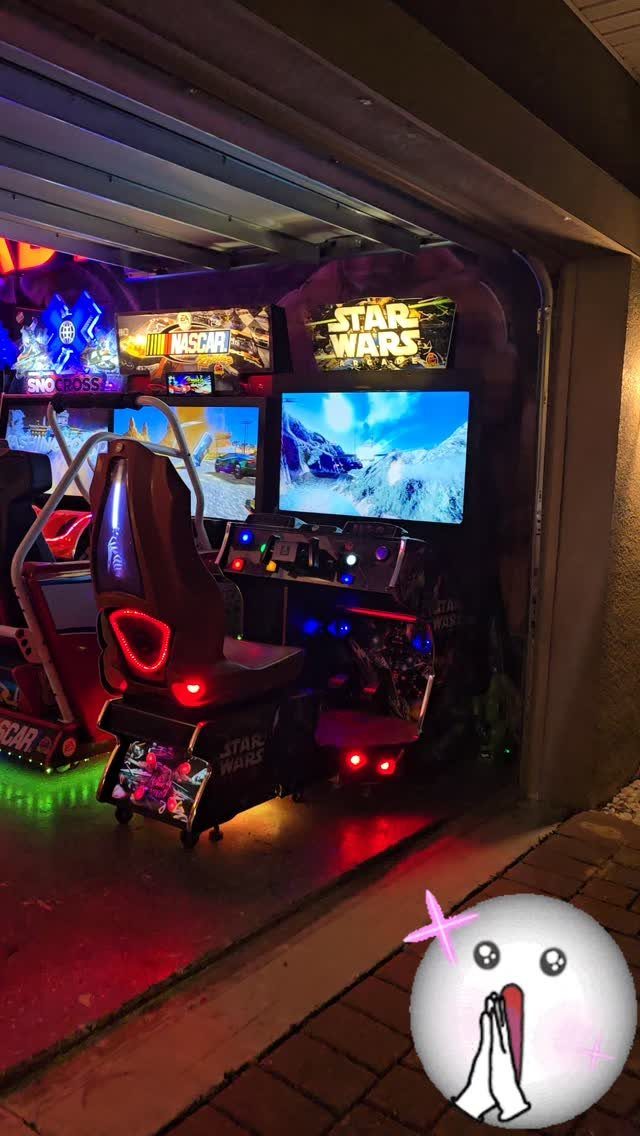 Gaming setup in a garage with racing simulator, monitors, and neon arcade machines.