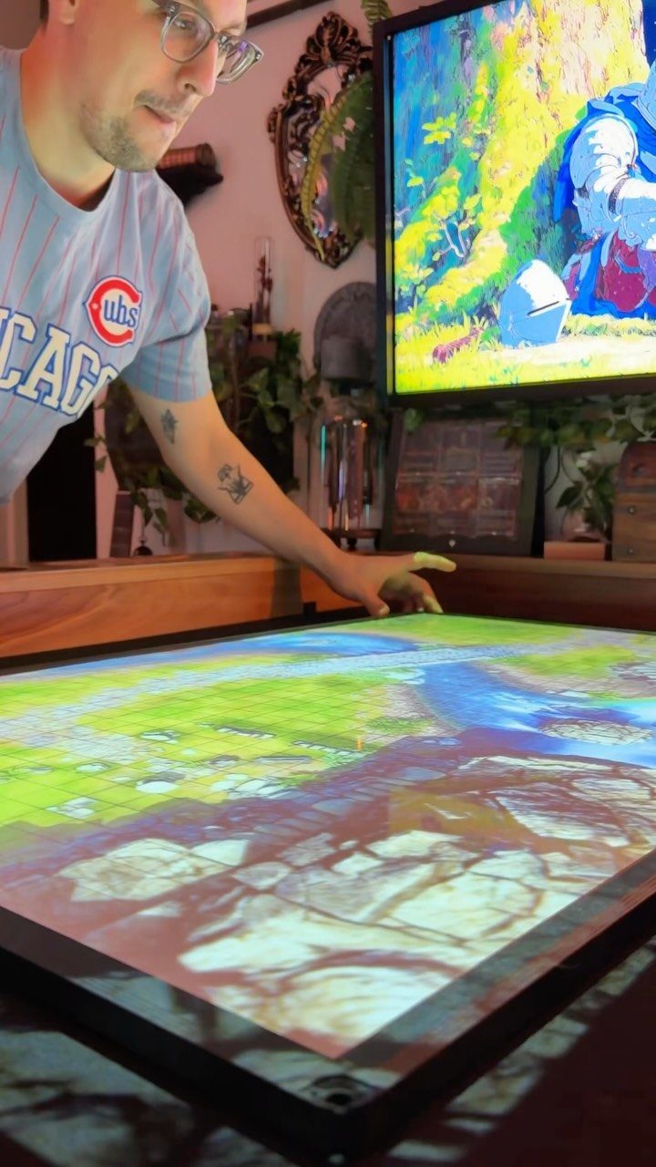 Man interacting with a large digital gaming table displaying a colorful landscape.