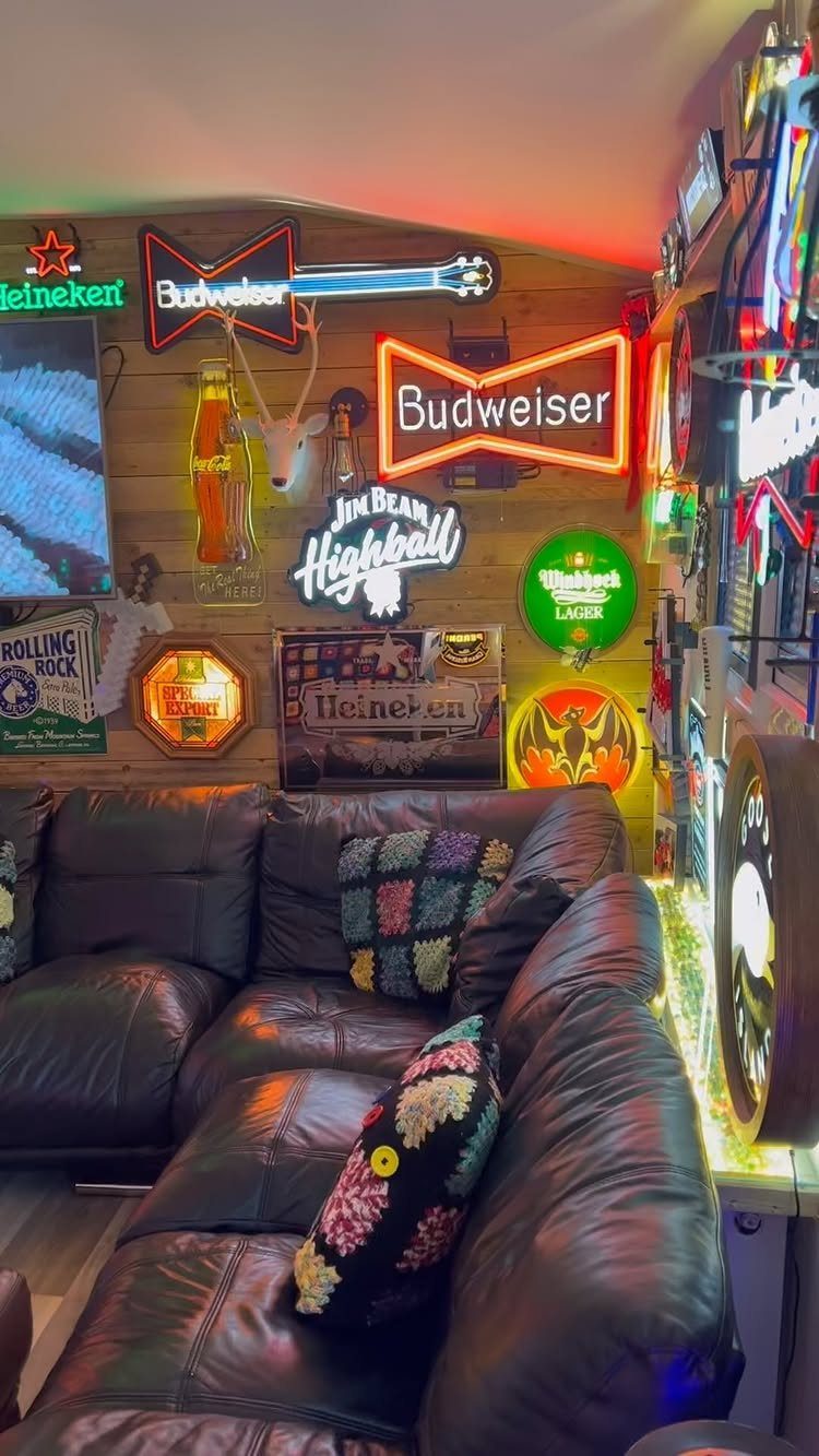 Neon beer signs illuminating a room with a dark leather sectional sofa.