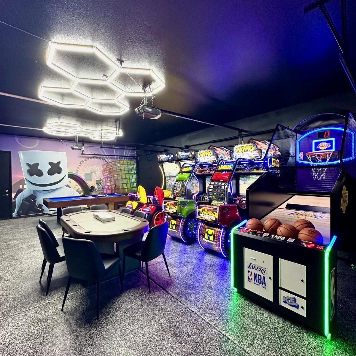 Modern adult game room with arcade machines, racing simulators, and blue ambient lighting.