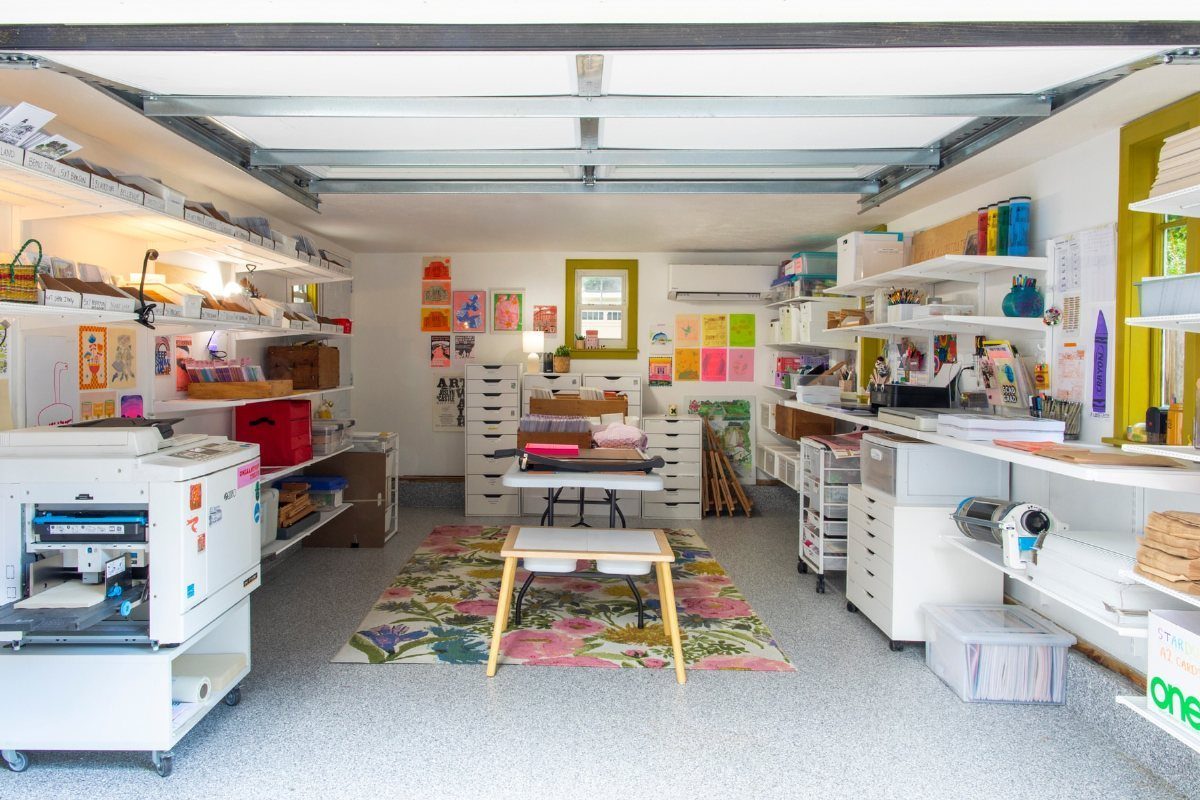 Converted garage art studio with white shelving, large printer, and colorful floral rug.