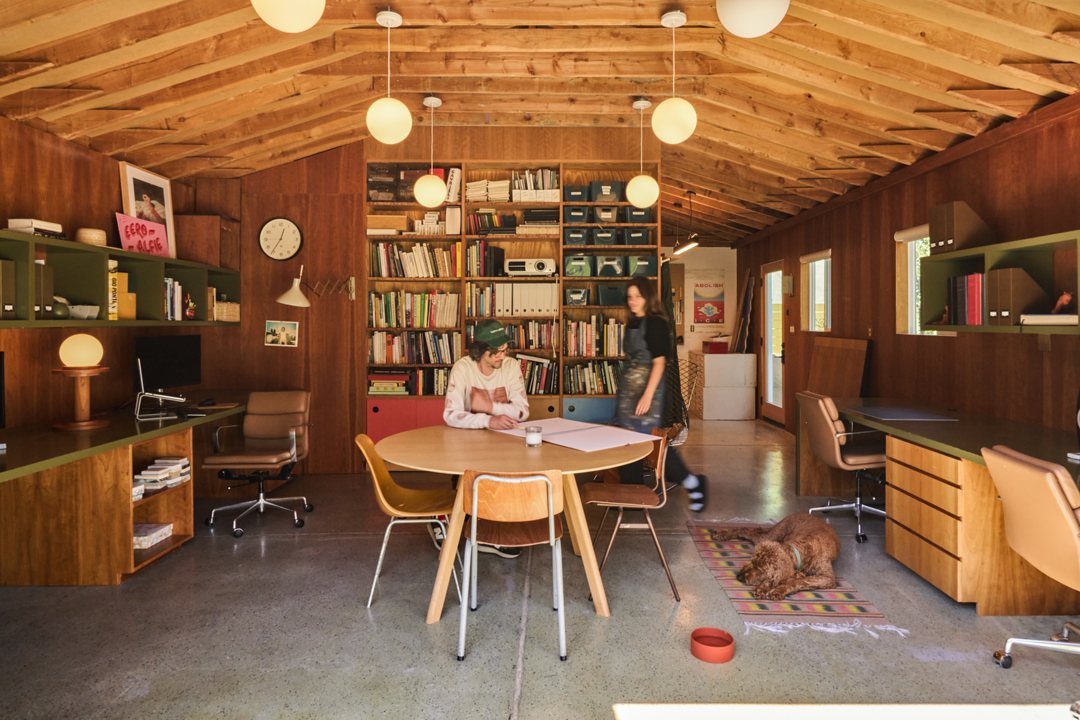 Wooden home office with a round table, desks, bookshelves, and globe pendant lighting.