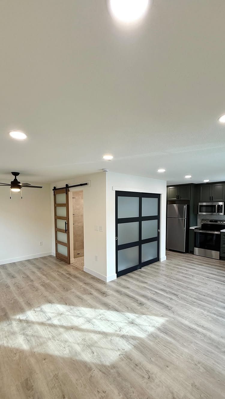 Modern converted living space with grey flooring, white walls, and a small kitchen.