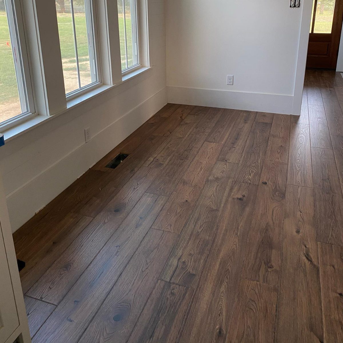 Brown hardwood flooring in a bright room with white walls and windows.