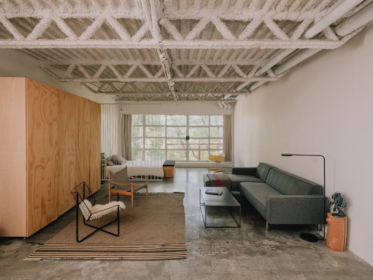 Modern open living space with grey sofa, wooden furniture, and industrial white ceiling.