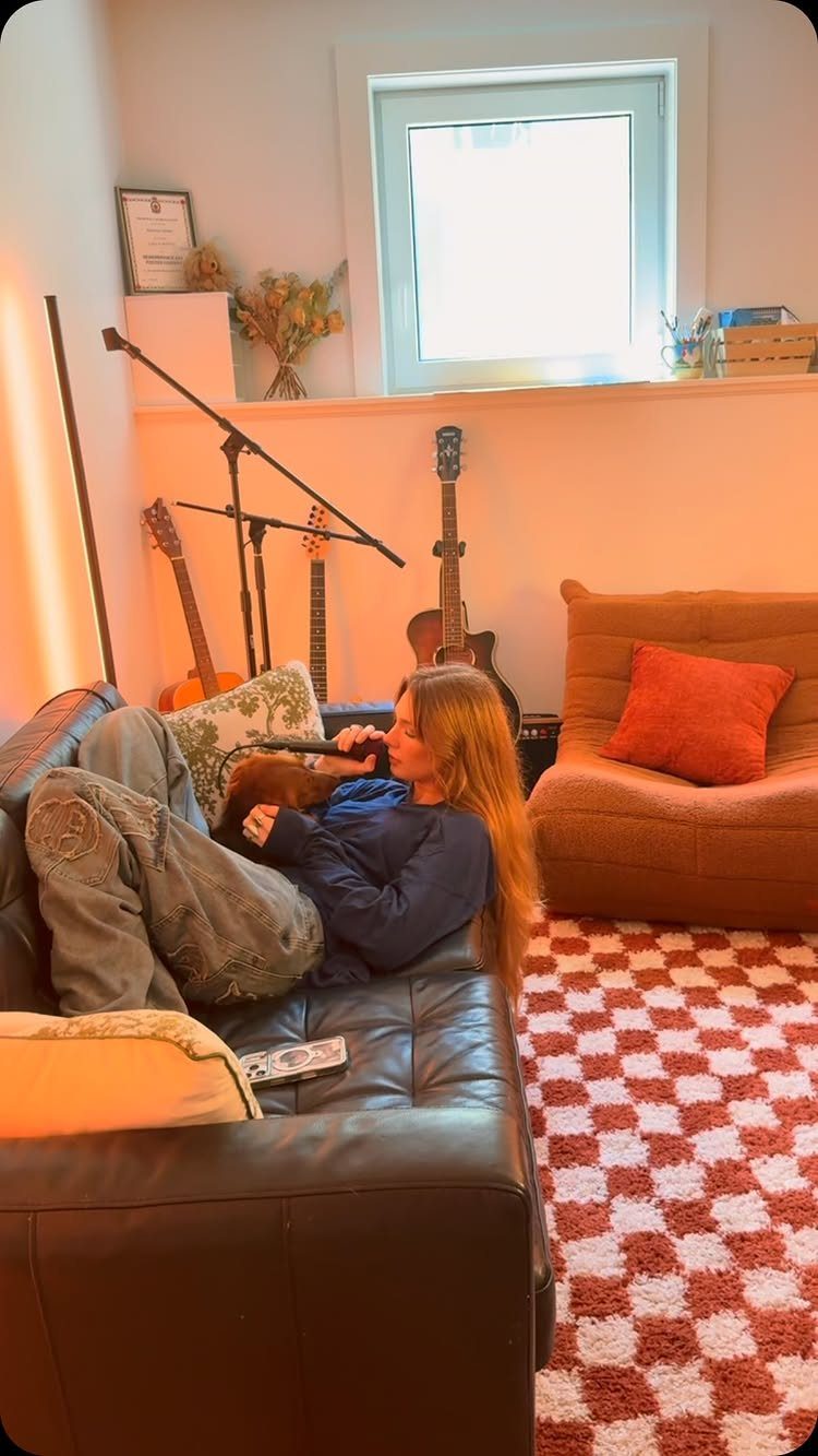 Person relaxing on a black leather sofa in a home music studio setting.