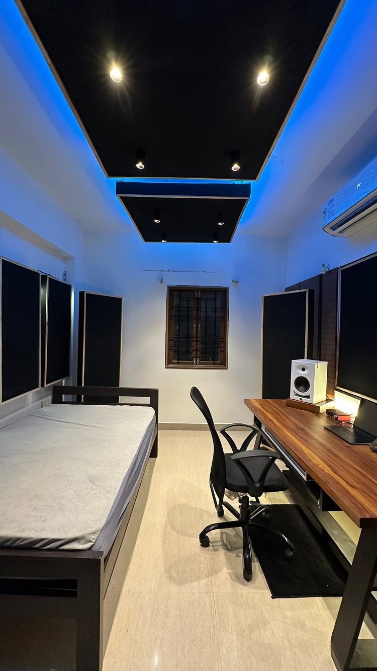 Home music studio with black acoustic panels, wooden desk, and blue LED ceiling lights.