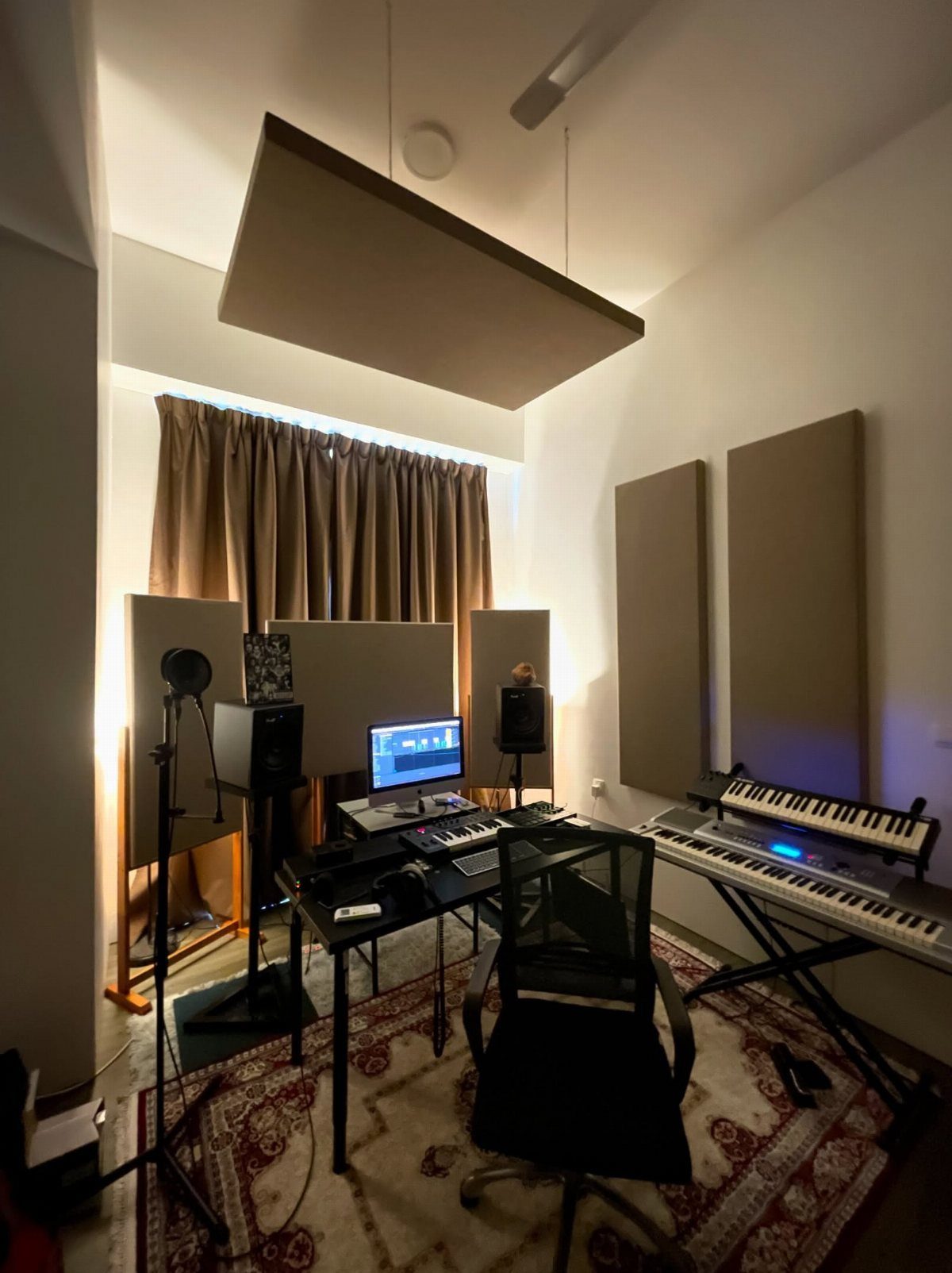 Home music studio with tan acoustic panels, computer desk, and electronic keyboards.