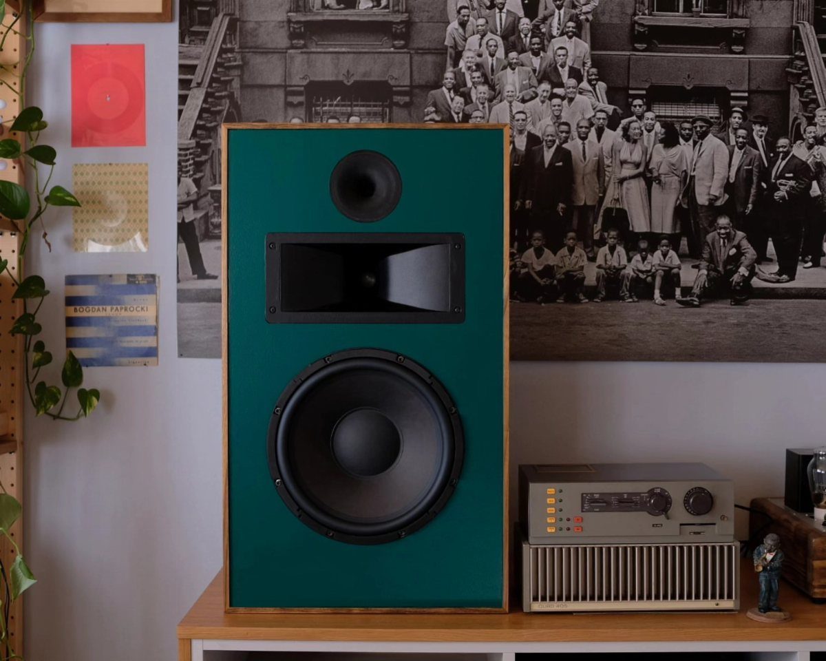 Large green speaker and vintage silver receiver on a wooden table against a wall.