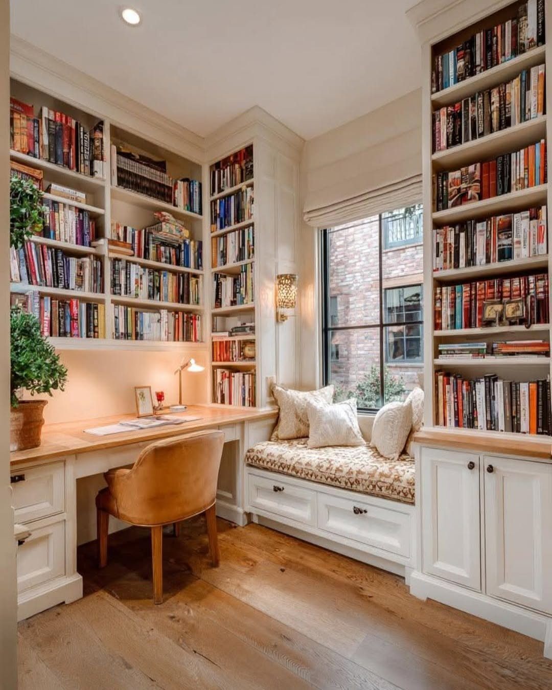 White built-in bookshelves and a desk with a window seat in a home office.