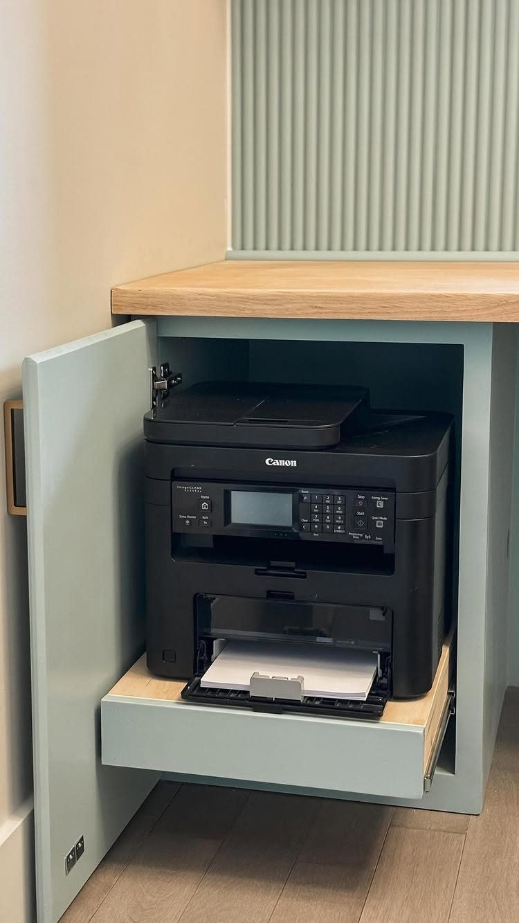 Black printer on a pull-out shelf inside light blue home office built-in cabinetry.