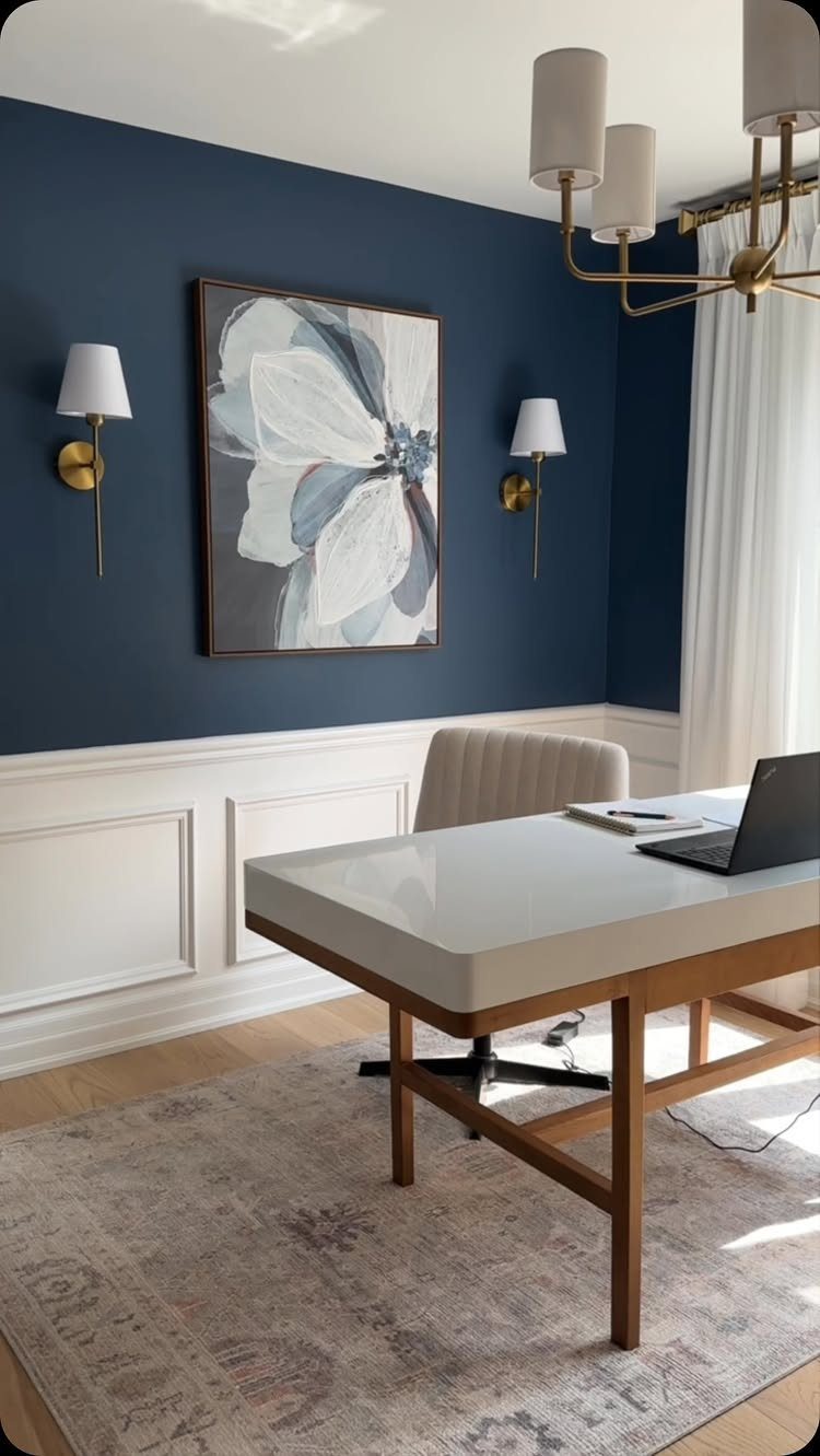 Navy blue accent wall with white wainscoting, floral art, and a modern desk.