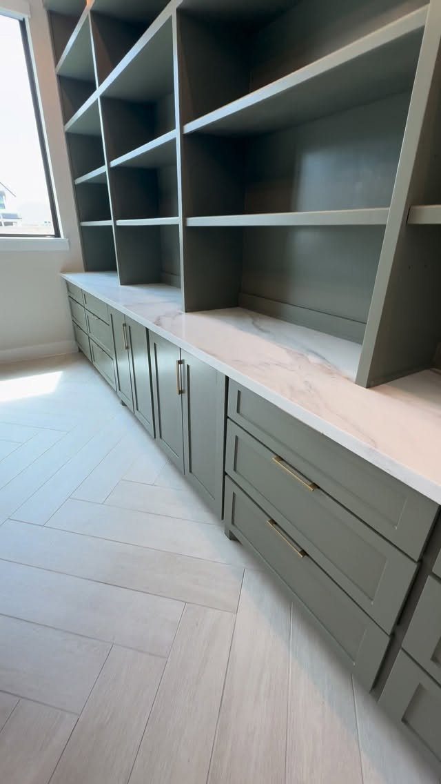 Grey built-in cabinets with open shelving and a white marble countertop on herringbone floors.