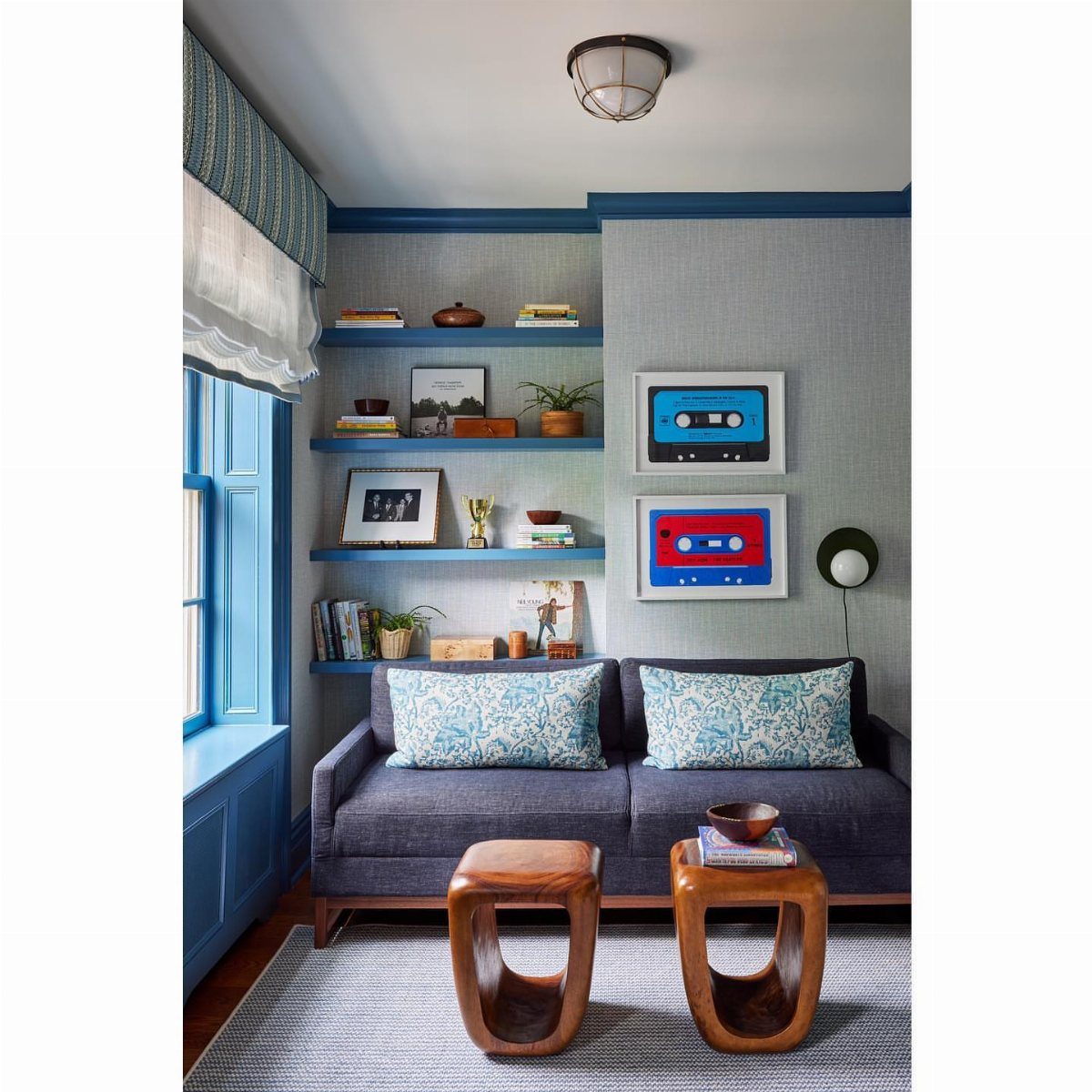 Grey sofa with patterned pillows and wooden side tables in a blue-themed office.
