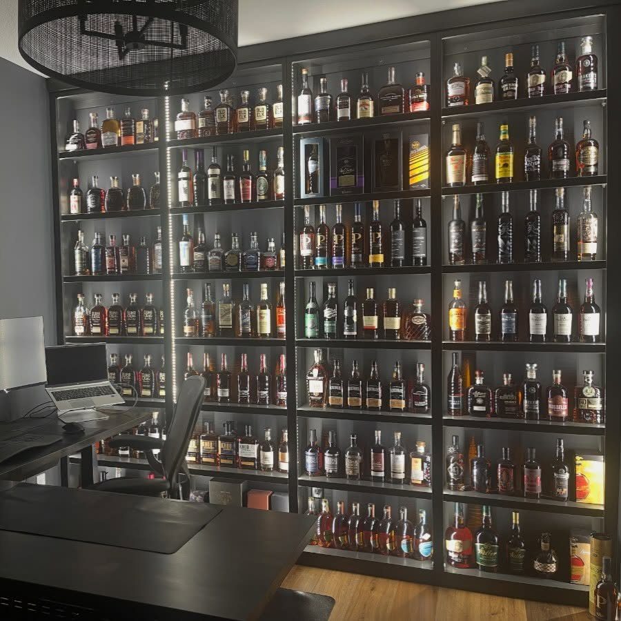 Large black shelving unit filled with liquor bottles in a modern home office.