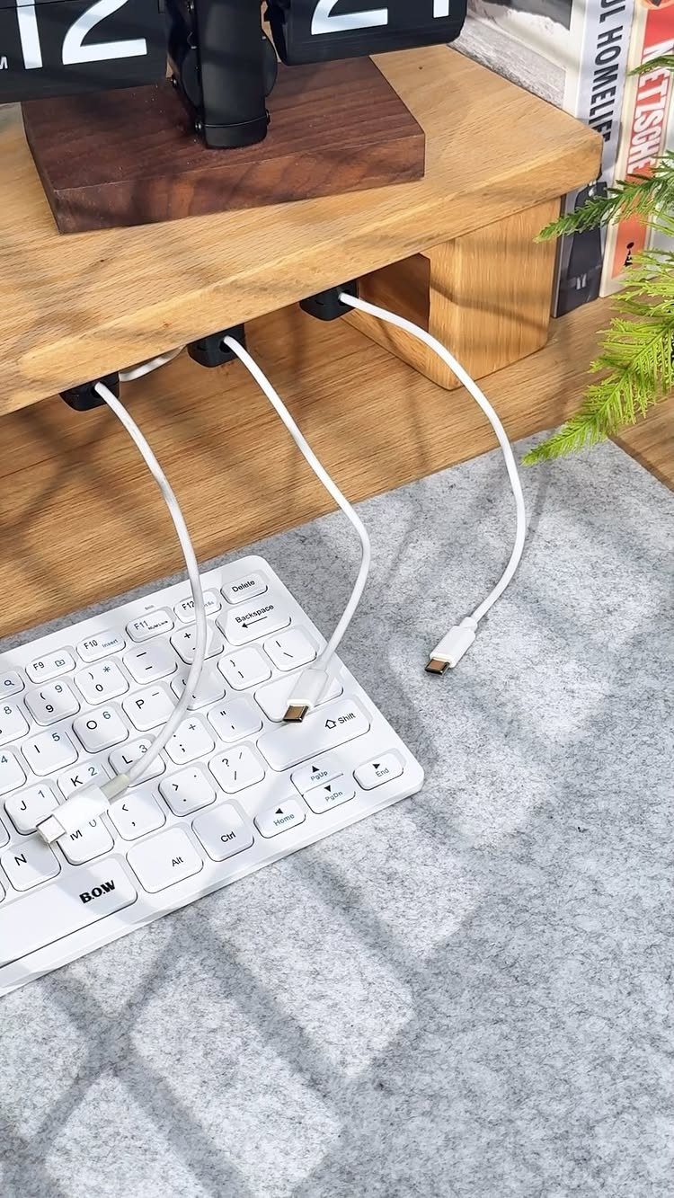 Black cable clips organizing white wires under a light wooden desk surface.