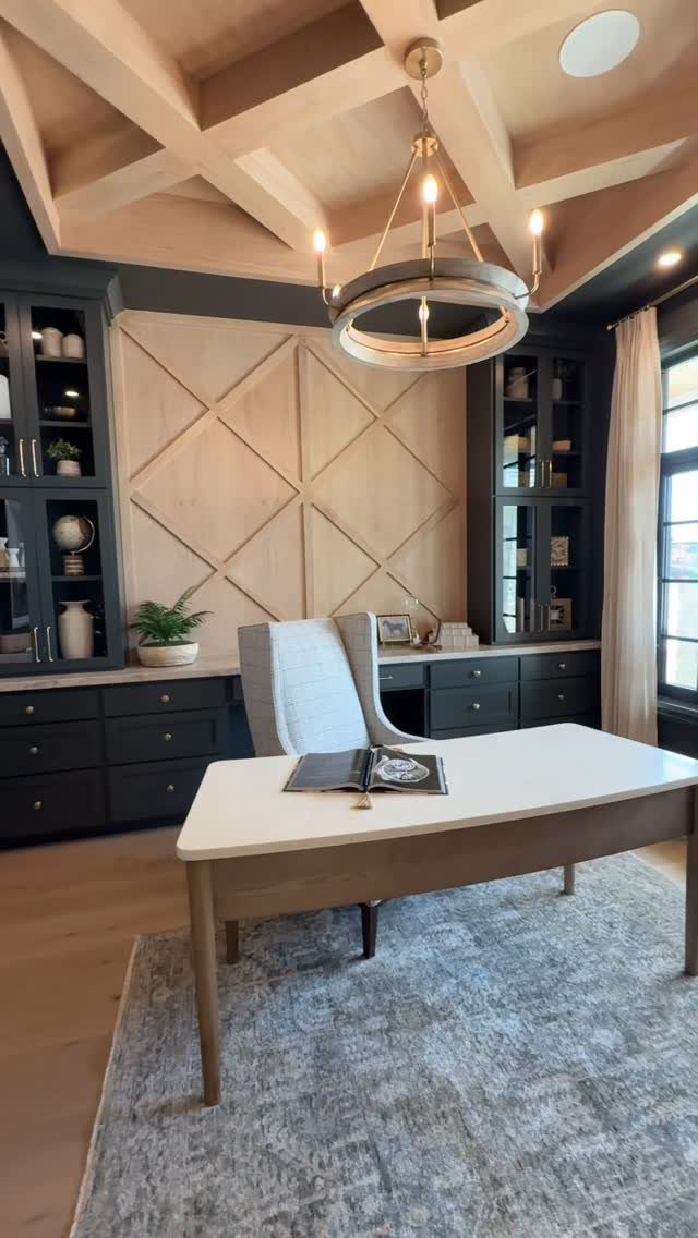 Elegant home office with a light desk, navy cabinets, and coffered wooden ceiling.