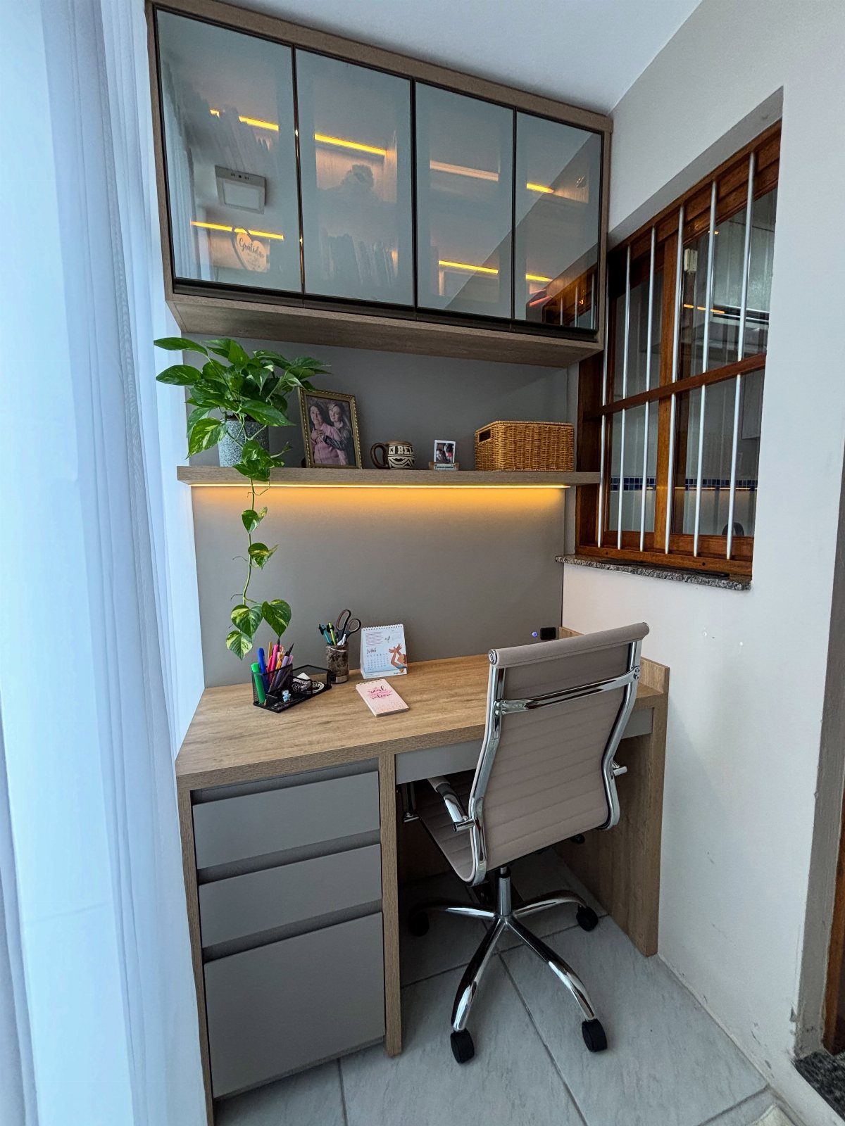 Modern home office desk with ergonomic chair, indoor plant, and overhead storage cabinets.
