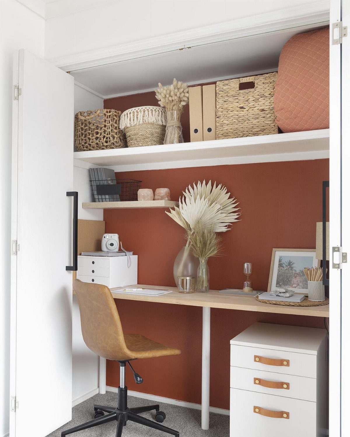 Closet home office with a light wood desk, tan chair, and terracotta wall.