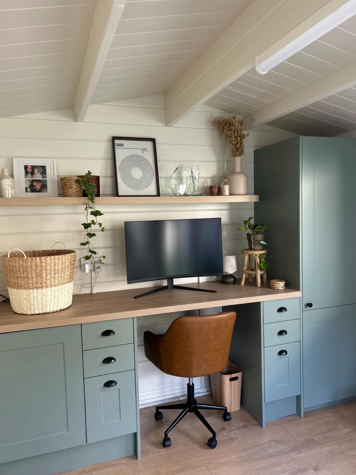 Sage green built-in desk with brown leather chair under a sloped white ceiling