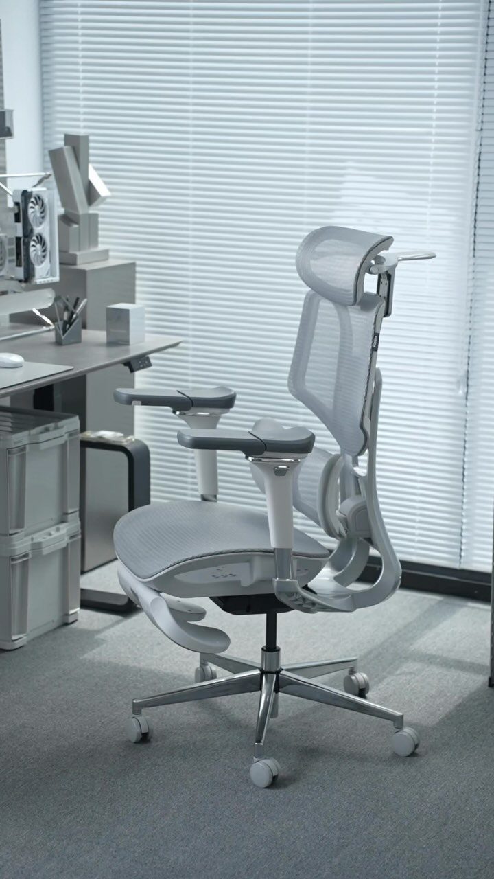 Grey ergonomic office chair with mesh back and headrest in a bright office