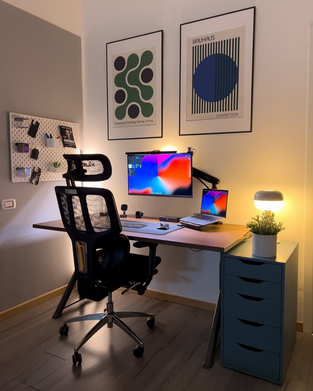 Home office desk with a glowing table lamp, monitor, and ergonomic black chair.