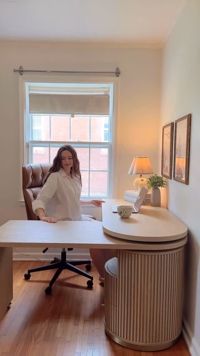 Woman sitting at a curved light-colored corner desk in a bright home office.