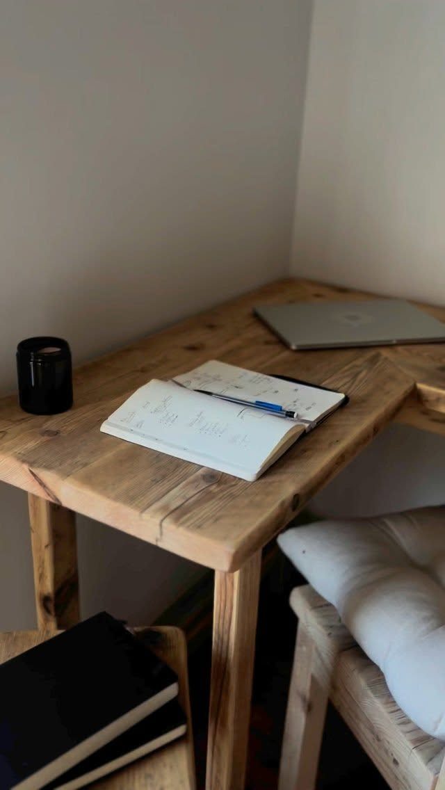 Wooden corner desk with a laptop, open notebook, and white cushioned chair.