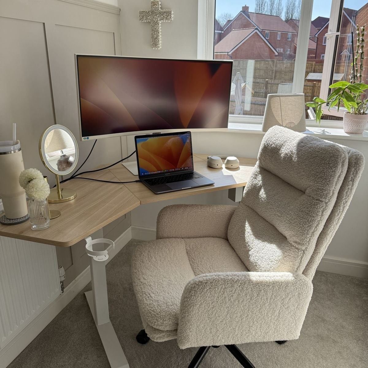 Light wood corner desk with a large monitor, laptop, and plush white chair.