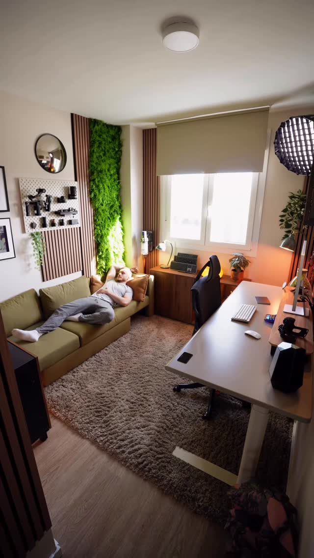 Home office with a white desk, brown rug, and a man resting on a green sofa.