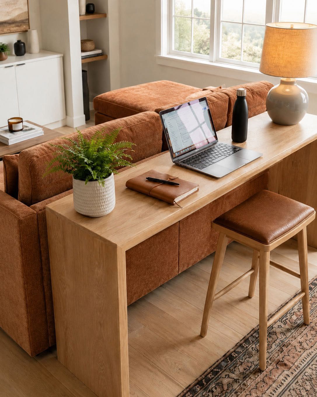 Wooden desk with laptop placed directly in front of a low brown sofa.