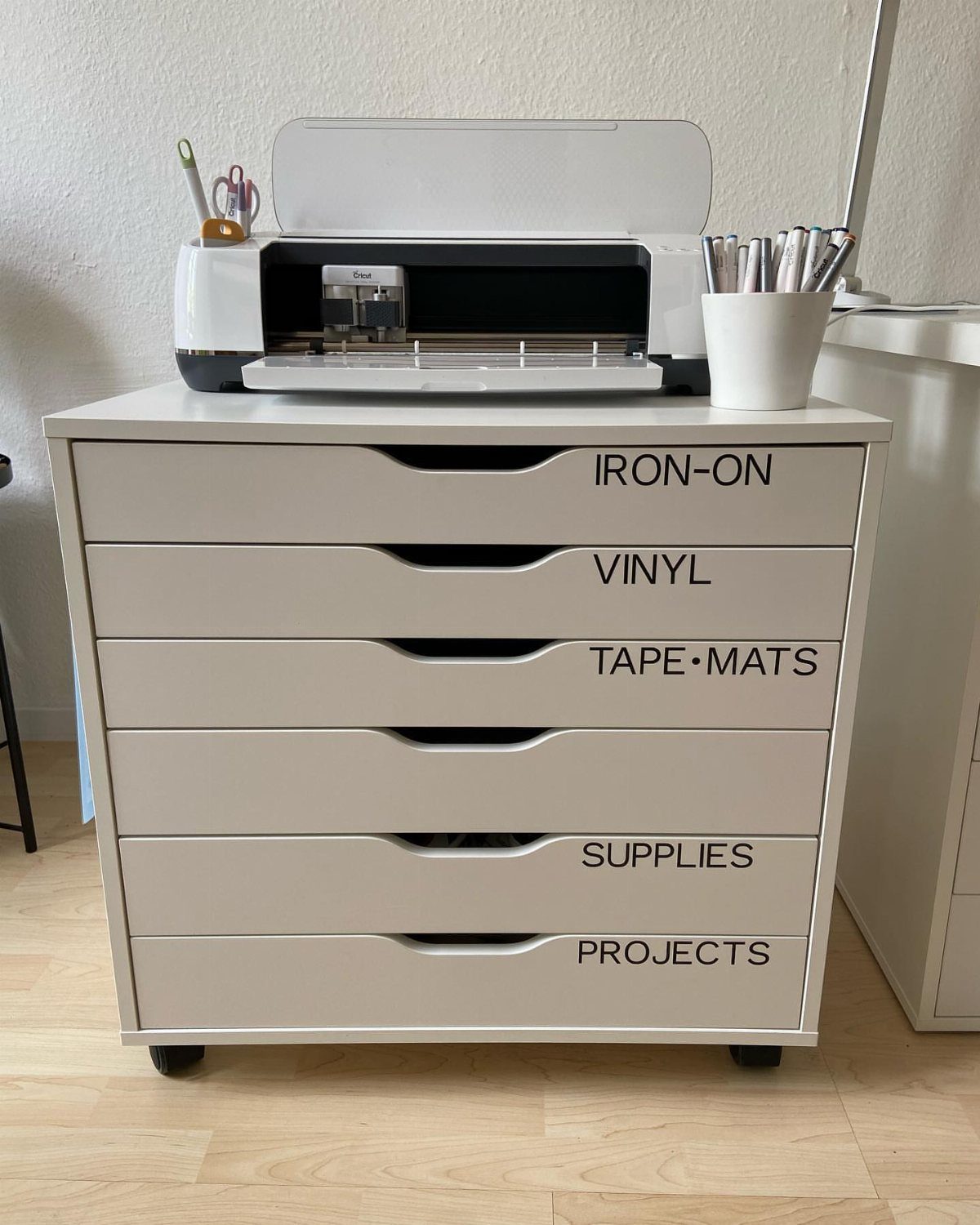 White IKEA Alex drawer unit with labels and a Cricut machine on top.