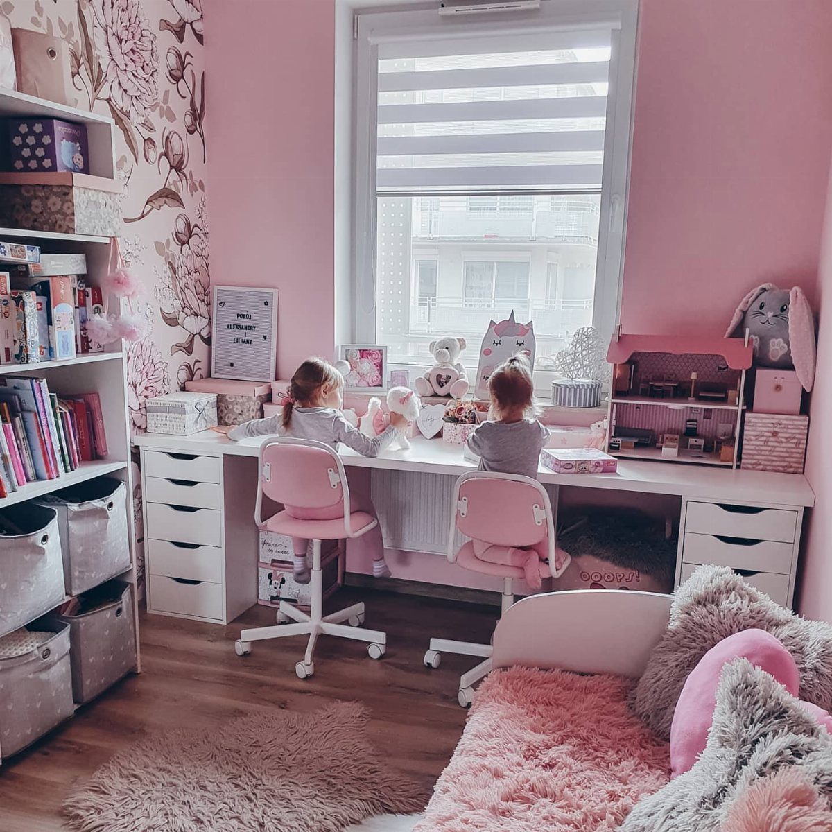 Two girls sitting at a white desk with Alex drawers in a pink room.