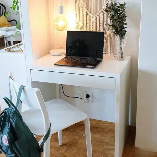 White small desk with laptop, lamp, and plant next to a white chair.