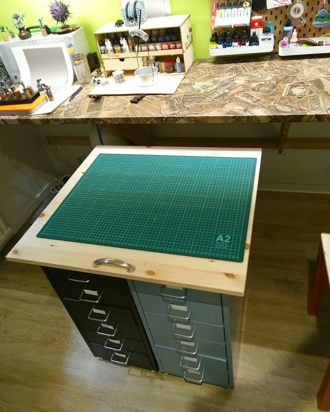 Two metal HELMER drawer units supporting a wooden tabletop with a green cutting mat.