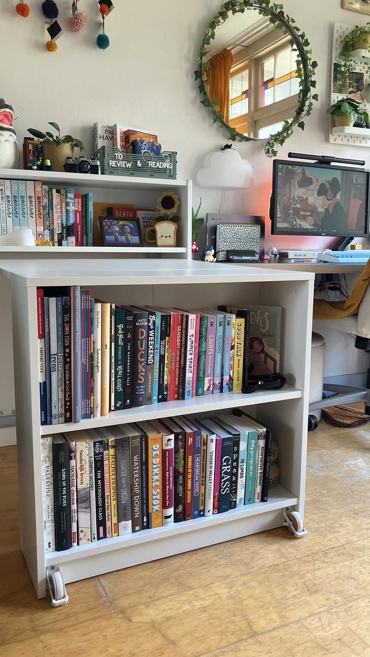 White IKEA bookcase on wheels filled with books next to a home office desk.