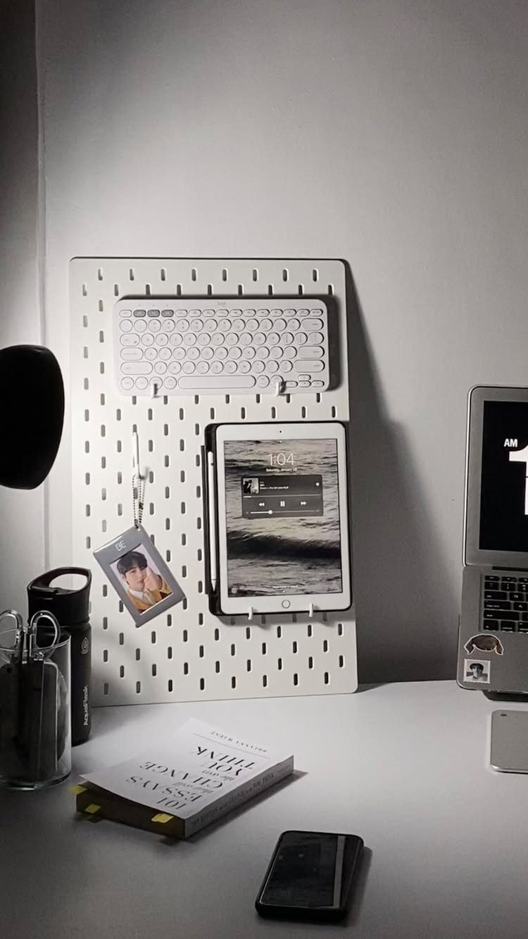 White desk setup with a pegboard holding a keyboard and tablet against a wall.