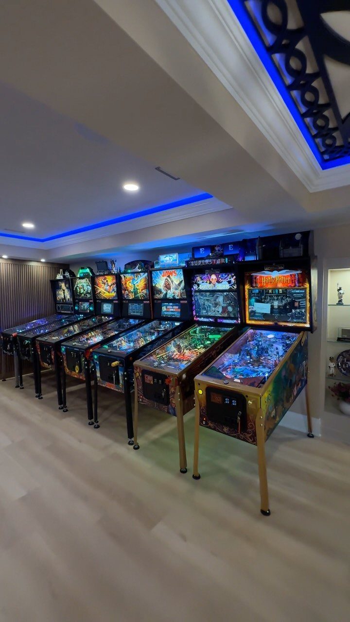 Row of colorful pinball machines in a room with blue LED ceiling lighting.